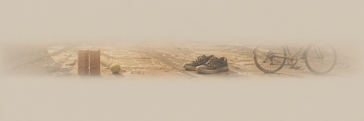 A faded, low-contrast horizontal banner-style scene showing a pair of dark sneakers, a bicycle wheel, a small green ball, and a brown box on a sandy ground.